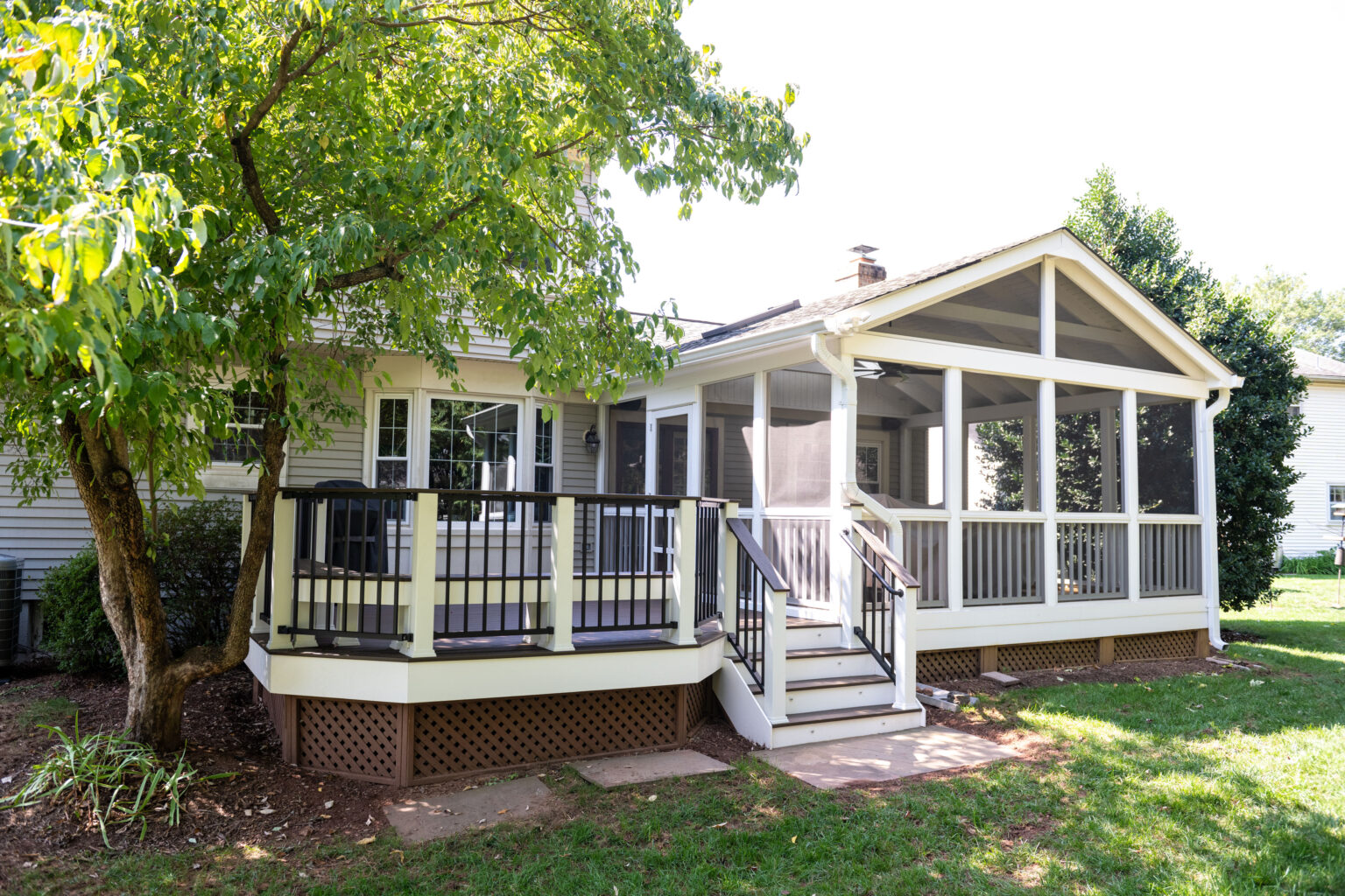 Image by Lesnick Photo A house with a screened-in porch and black railing, surrounded by grass, a stone path, and trees.