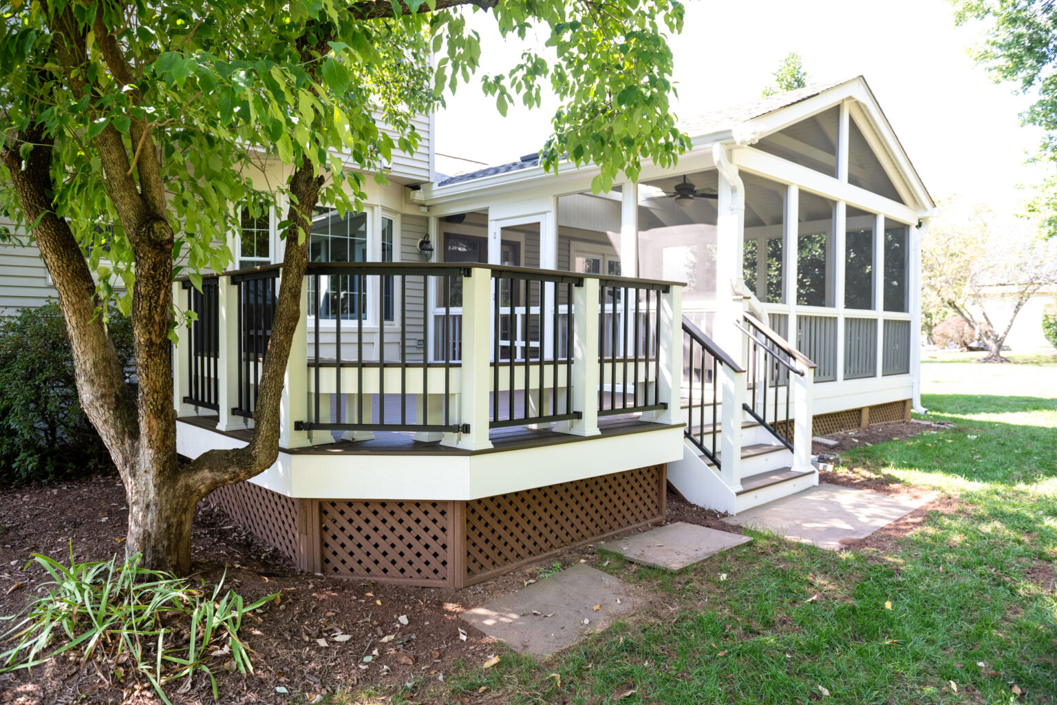 Image by Lesnick Photo A house with a screened porch and adjacent deck, surrounded by greenery and lawn.