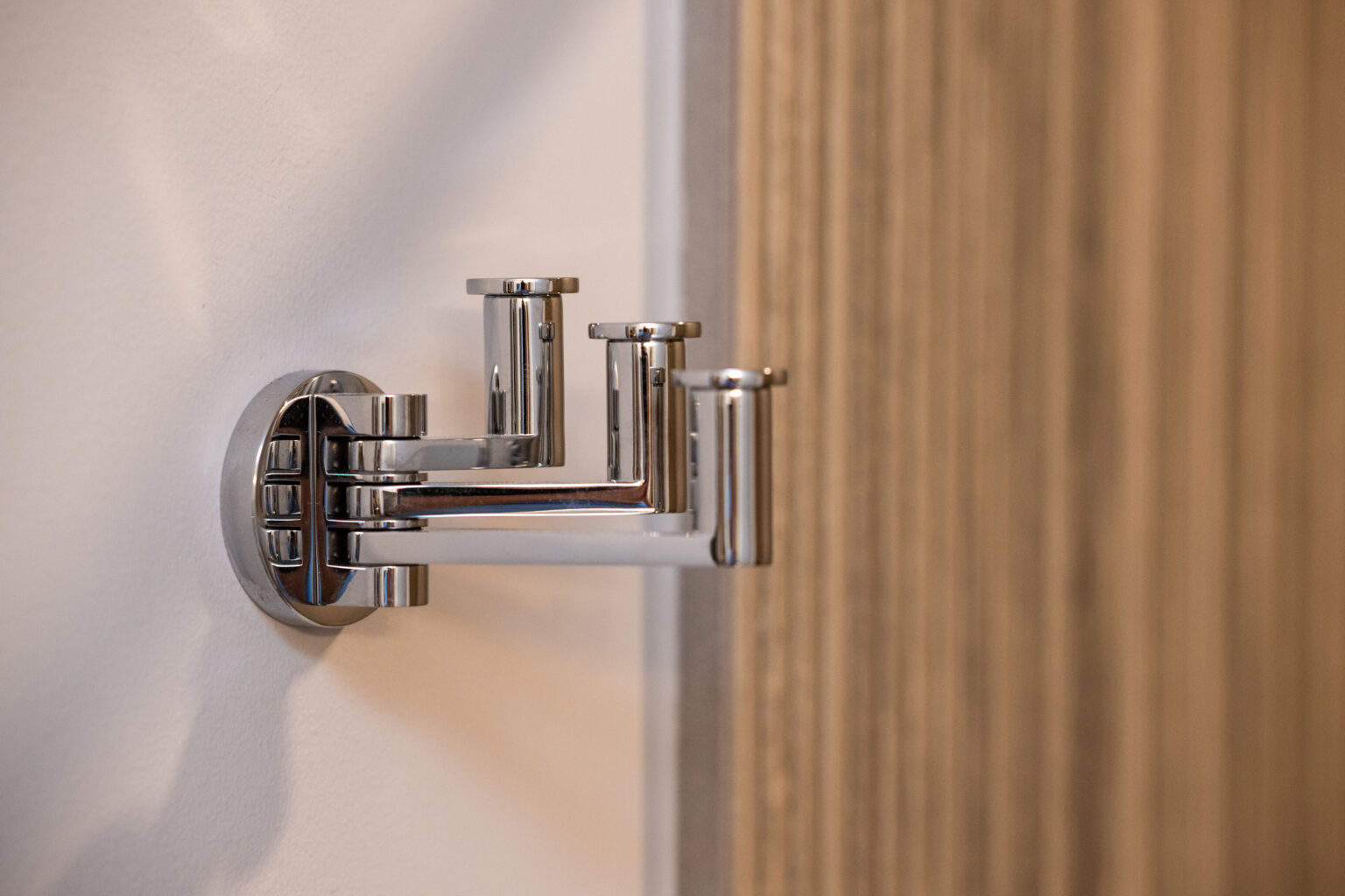 Image by Lesnick Photo A chrome wall-mounted multi-hook rack is attached to a white wall, with wooden paneling visible in the background.