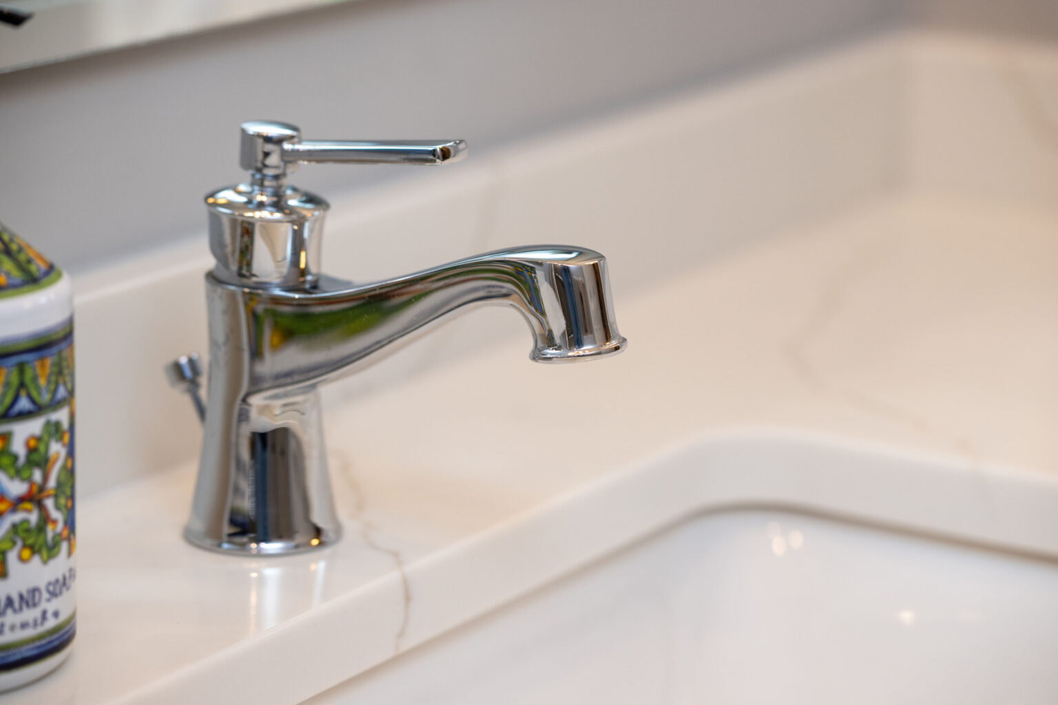 Image by Lesnick Photo A chrome bathroom faucet is installed on a marble countertop beside a decorative soap dispenser.