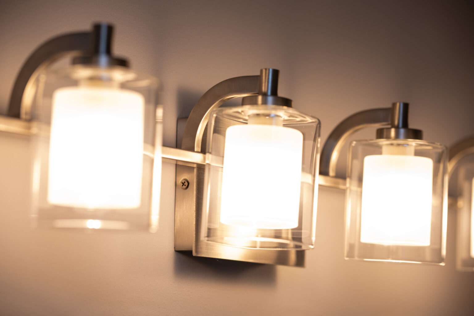Image by Lesnick Photo Close-up of a row of modern wall-mounted light fixtures with frosted glass shades and metallic bases, illuminating a softly lit room.