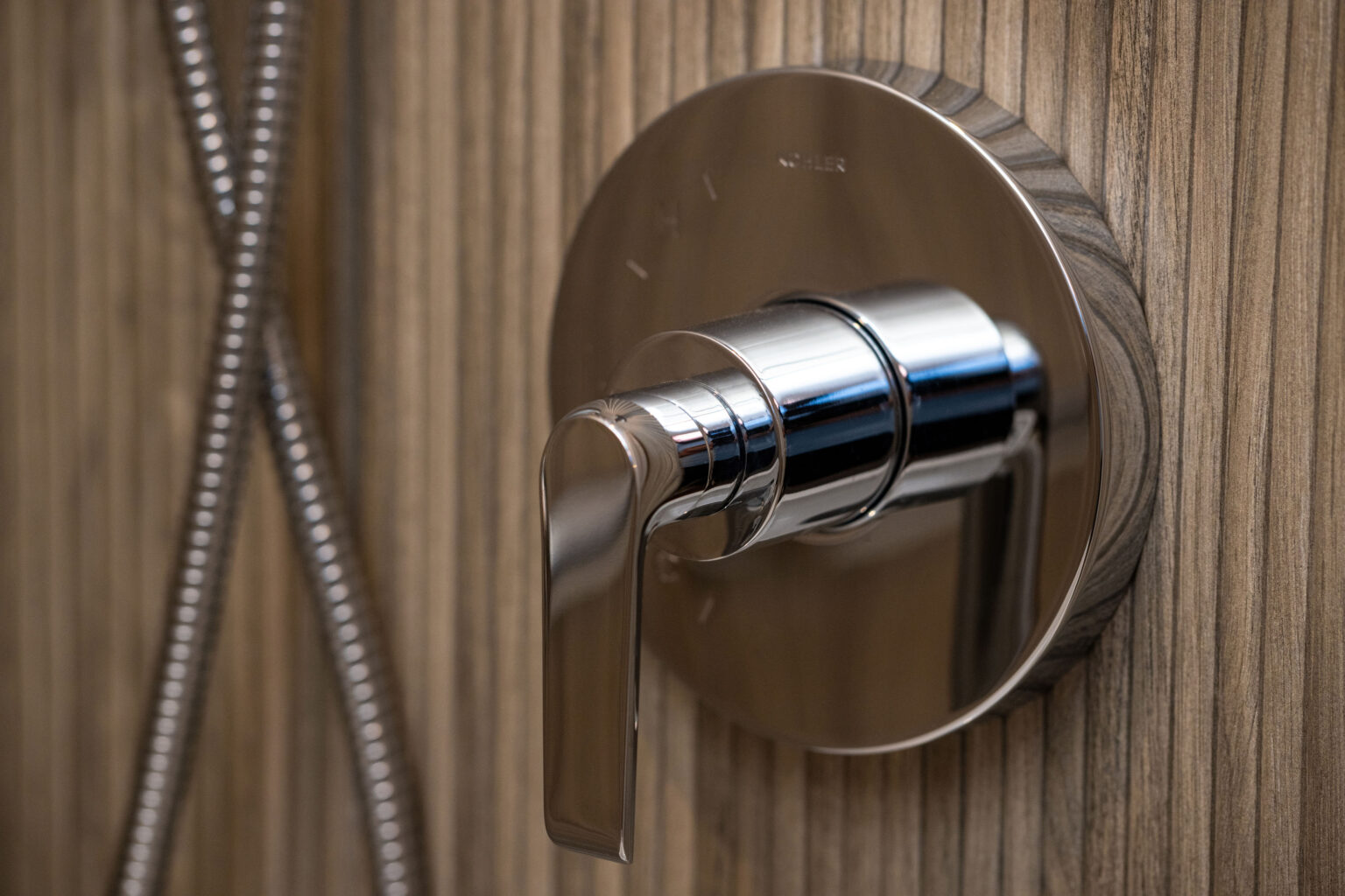 Image by Lesnick Photo Close-up of a chrome shower valve and handle on a textured wooden wall background.