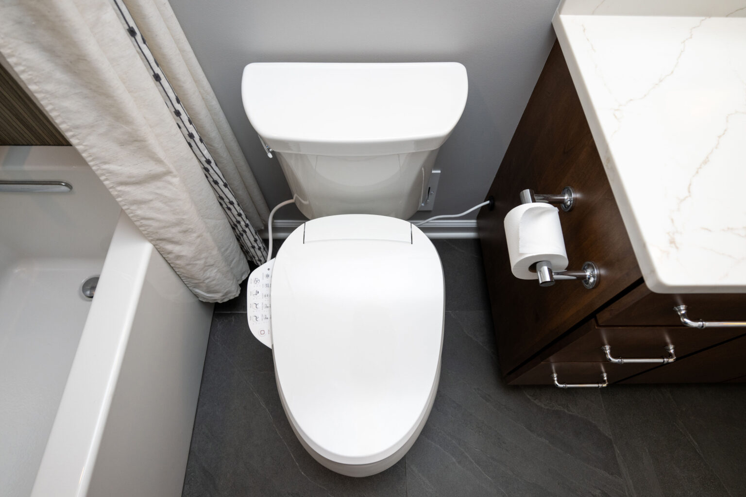 Image by Lesnick Photo Top view of a modern bathroom layout featuring a white toilet with a bidet attachment, adjacent to a bathtub, and a wooden vanity with a marble countertop.
