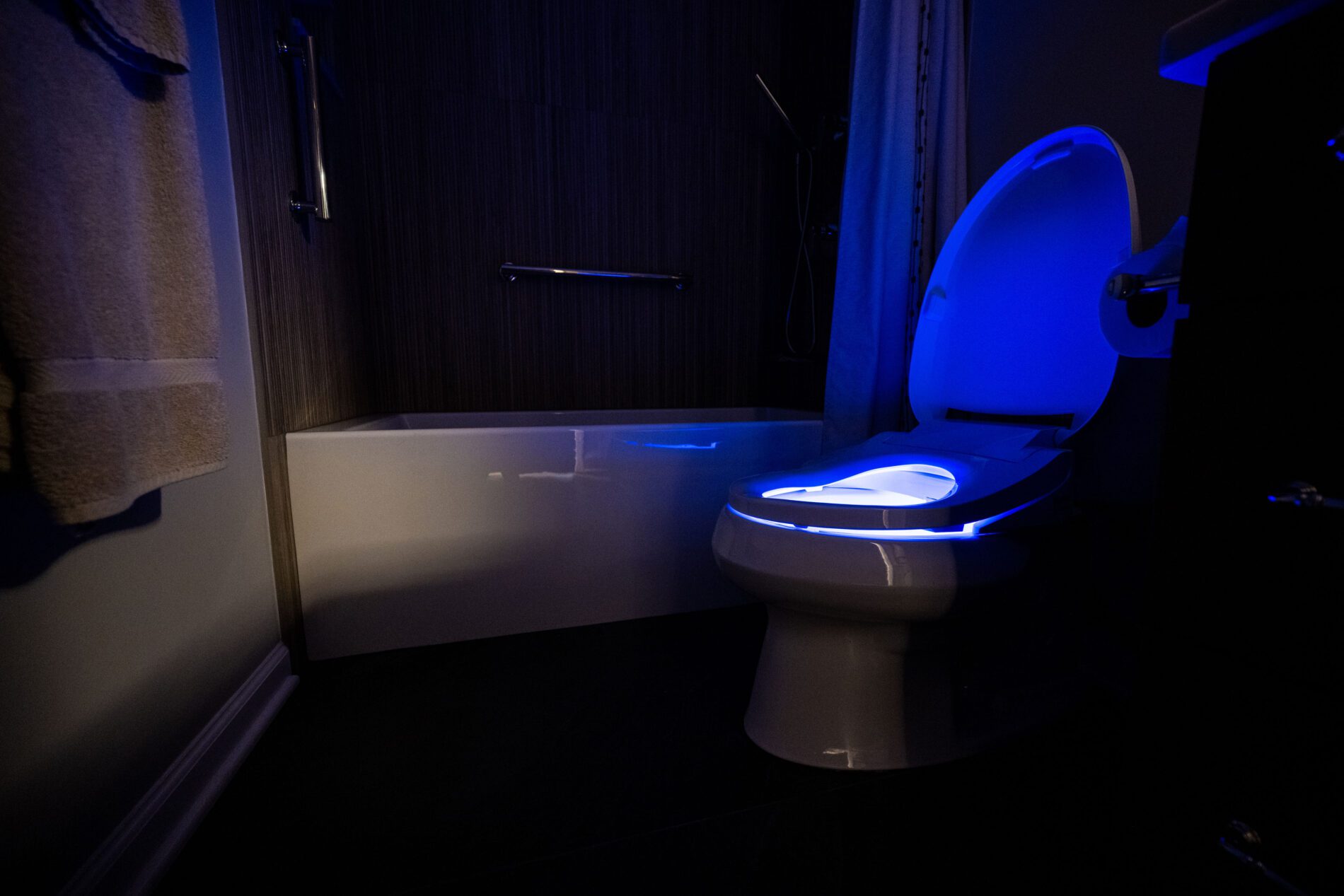 A bathroom with a bathtub and a toilet illuminated by blue LED lighting in a dimly lit setting.