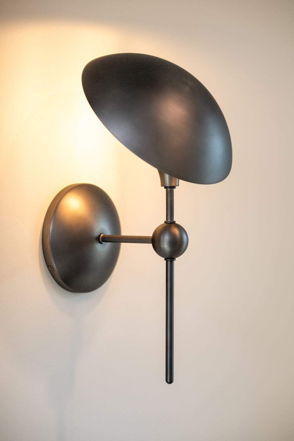 Modern black metal wall sconce with a round backplate and an oval-shaped shade mounted on a light-colored wall.