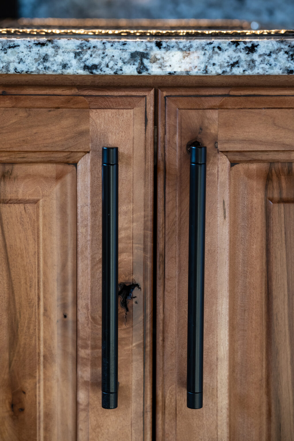 Close-up of two wooden cabinet doors with long black metal handles beneath a granite countertop.