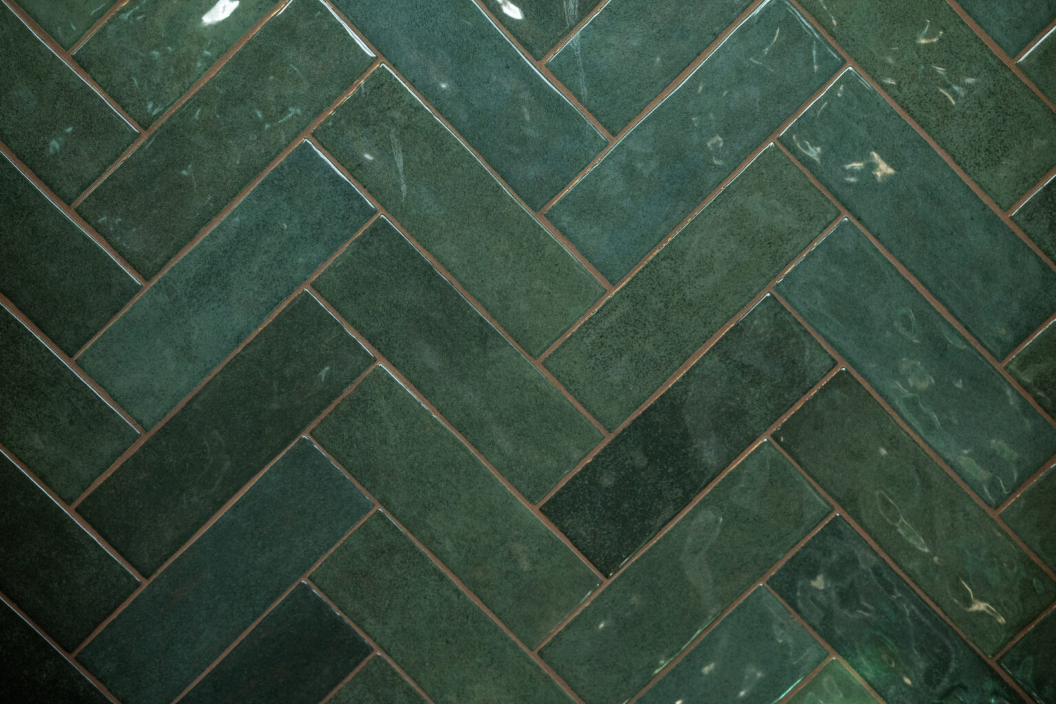 Close-up of green ceramic tiles arranged in a herringbone pattern with visible grout lines.