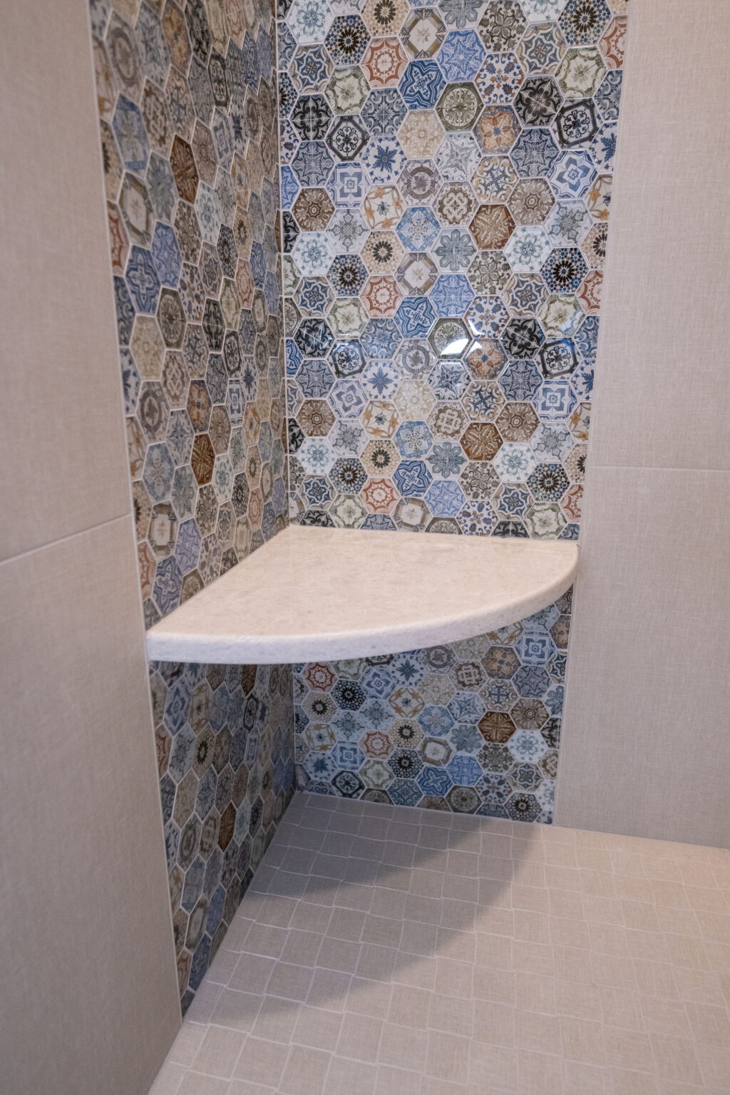 A shower corner with a small triangular shelf, featuring colorful hexagonal tile patterns on the walls and a light beige tiled floor.