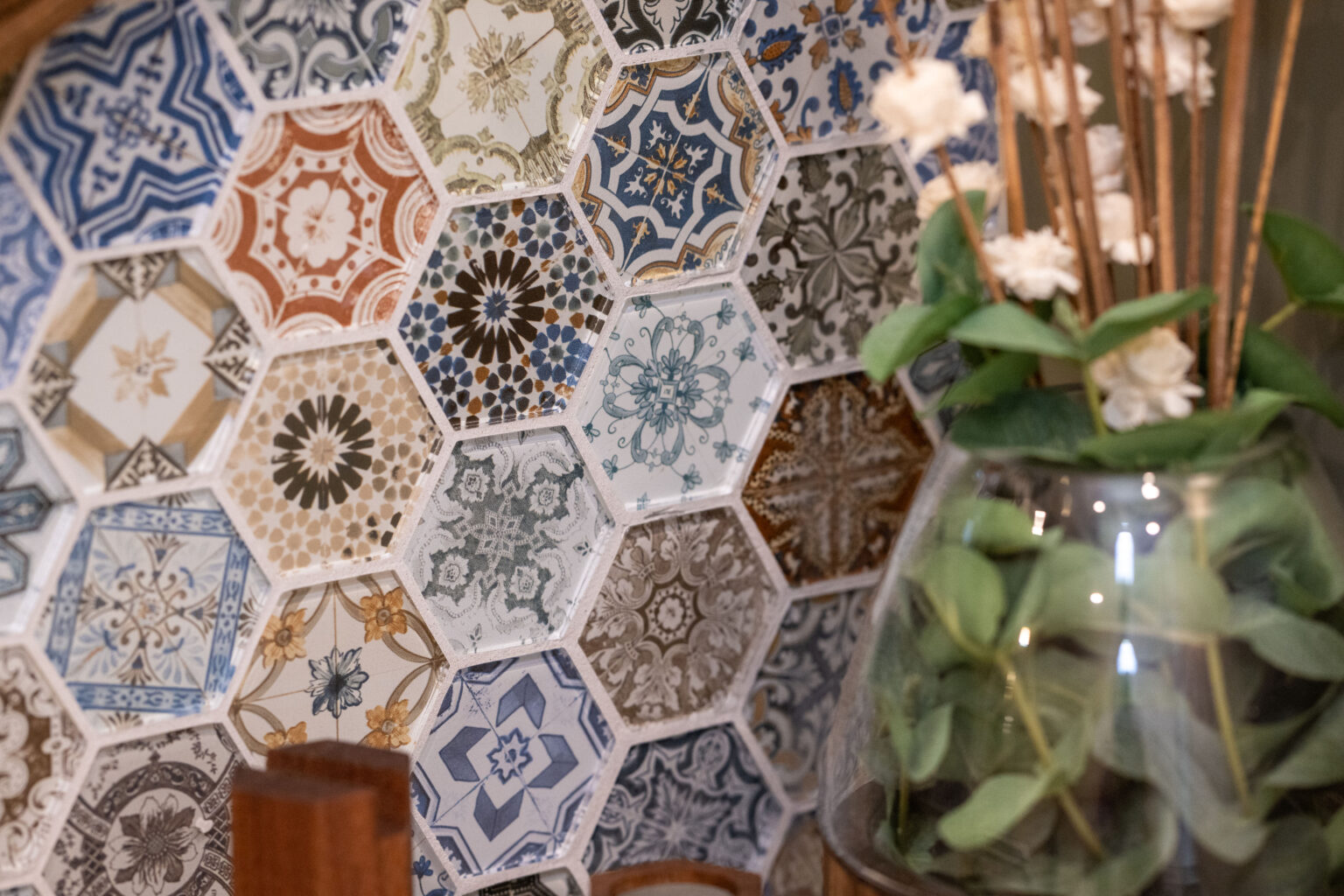 Decorative hexagonal tiles with intricate patterns are displayed next to a glass vase containing green leaves and dried flowers.