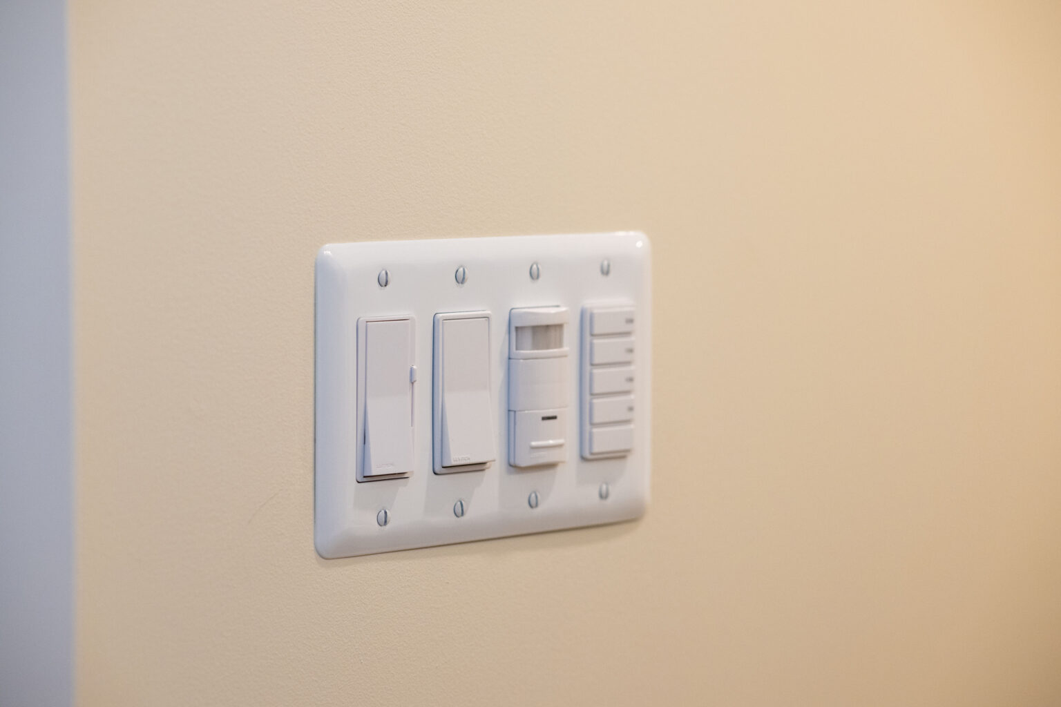 Four white light switches are mounted on a beige wall.