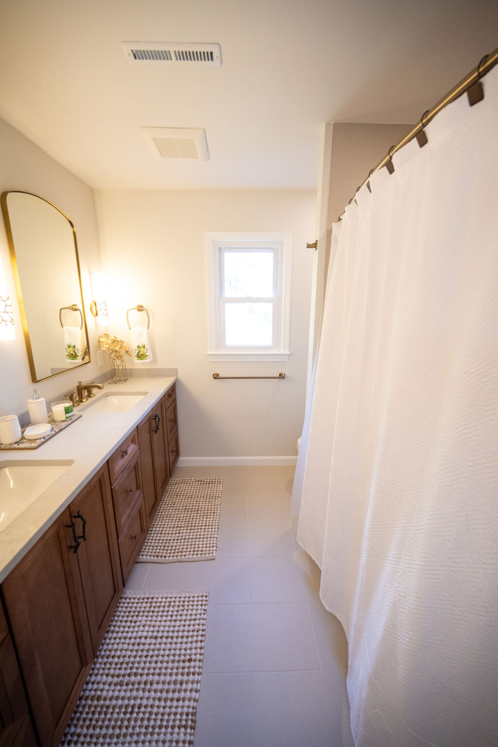Modern bathroom with a double sink vanity, wooden cabinets, two wall mirrors, white shower curtain, and two patterned rugs on the floor.