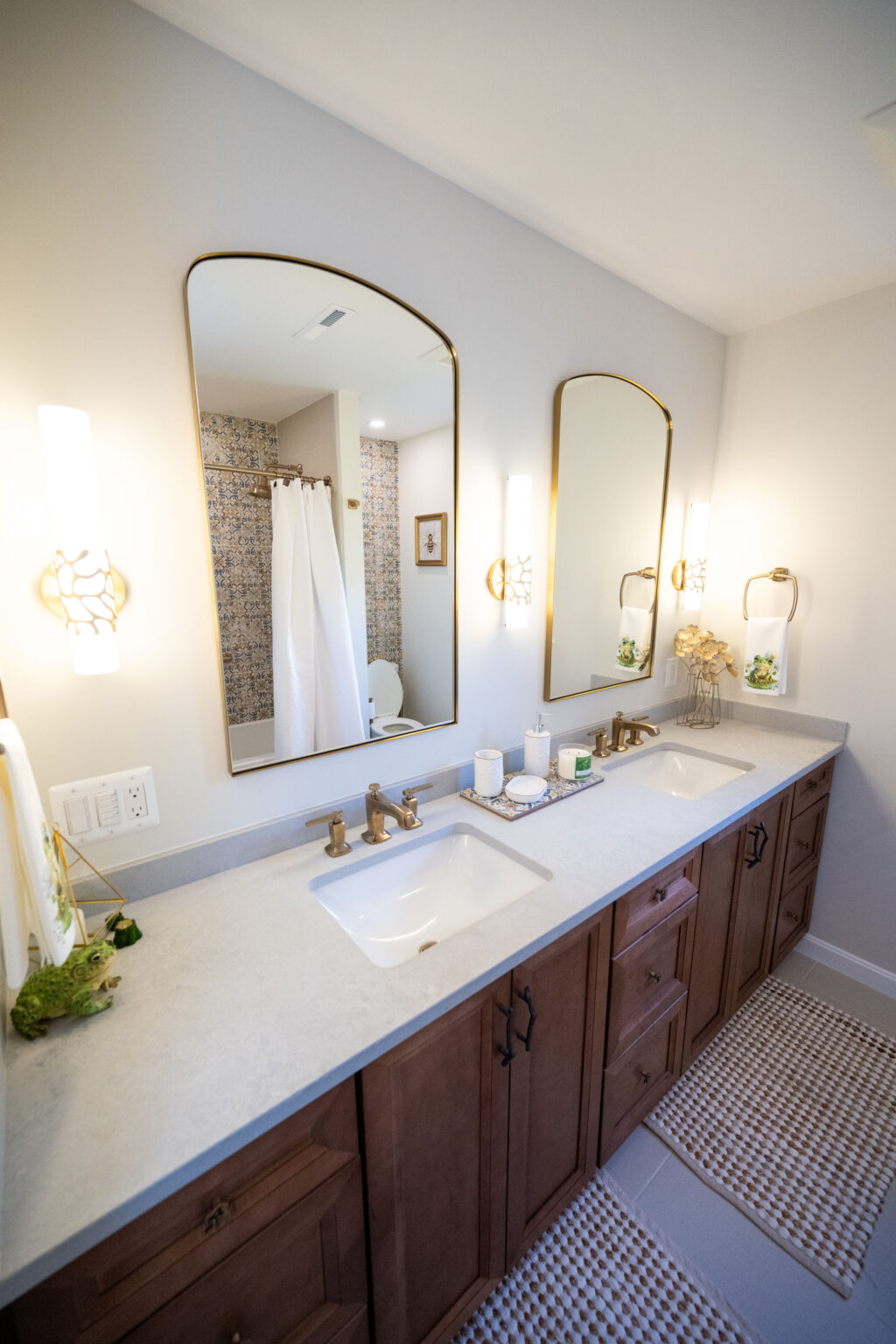 Bathroom with a double sink vanity, large mirrors, wall-mounted lights, and brown cabinets. A shower with a white curtain is in the background.