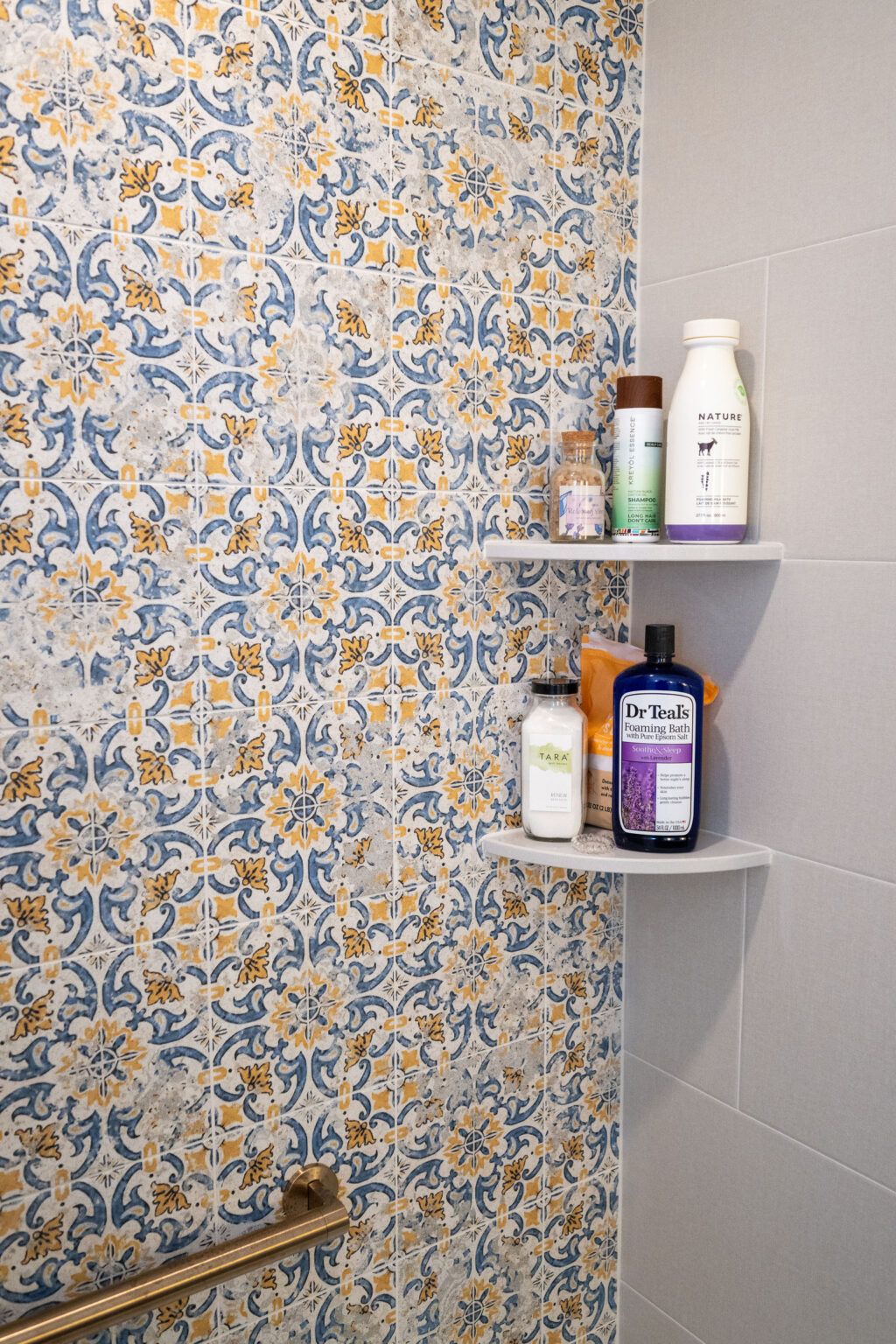 Shower with blue and orange floral-patterned tiles, two corner shelves holding various bath products.