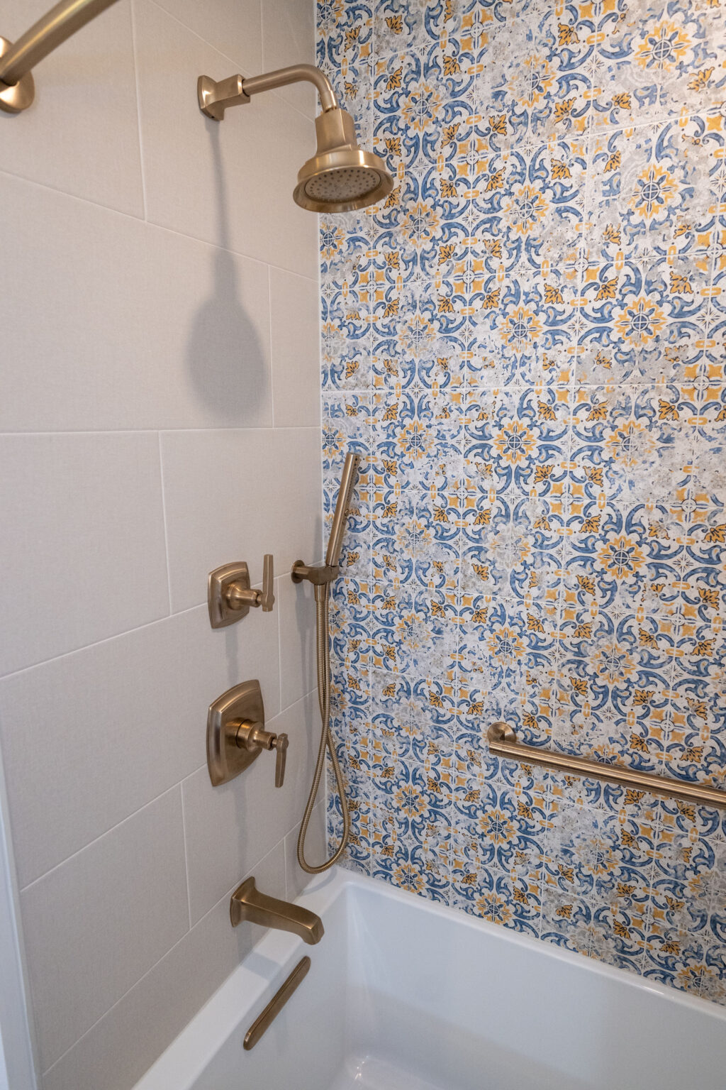Bathroom with a white bathtub, bronze fixtures, and a showerhead. The wall features a decorative blue and yellow tile pattern.