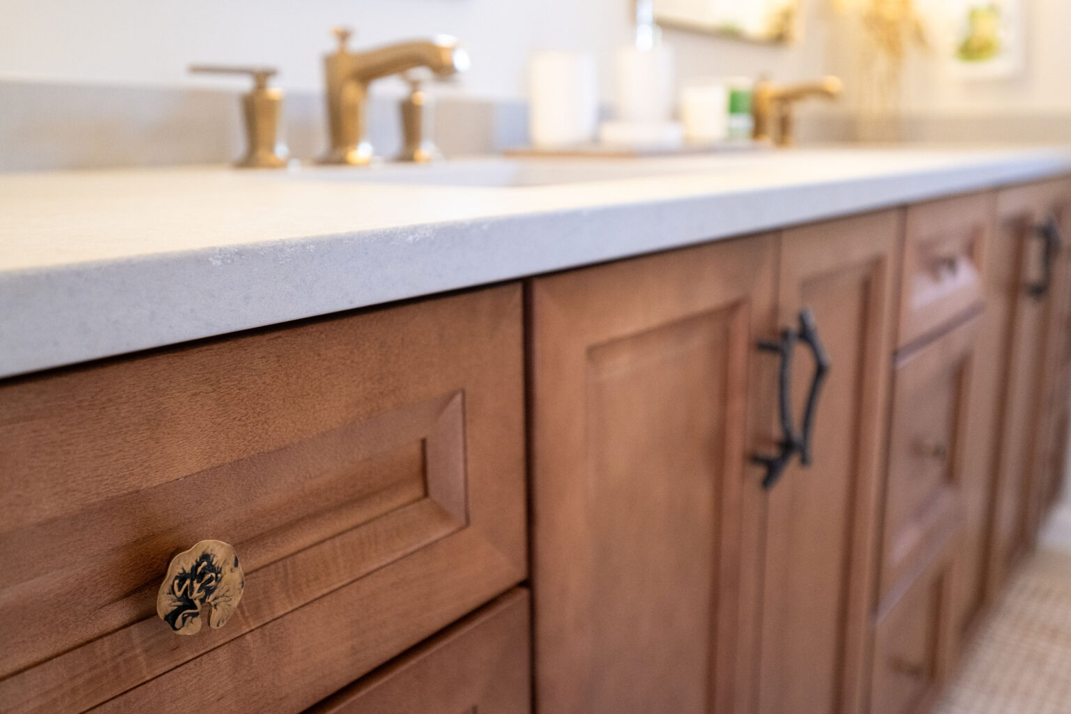 Bathroom vanity with wooden cabinets, a light countertop, and gold faucet fixtures.