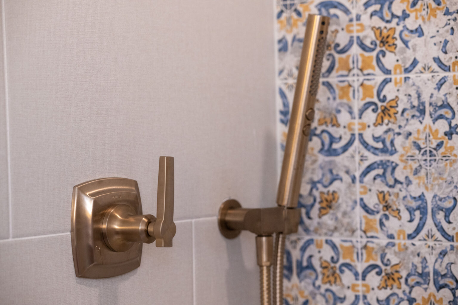 A bronze shower handle and wand mounted on a wall with blue and orange patterned tiles.