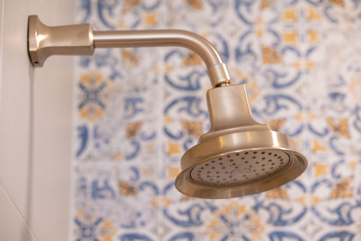 Close-up of a metallic showerhead attached to a wall with blue and orange patterned tiles in the background.