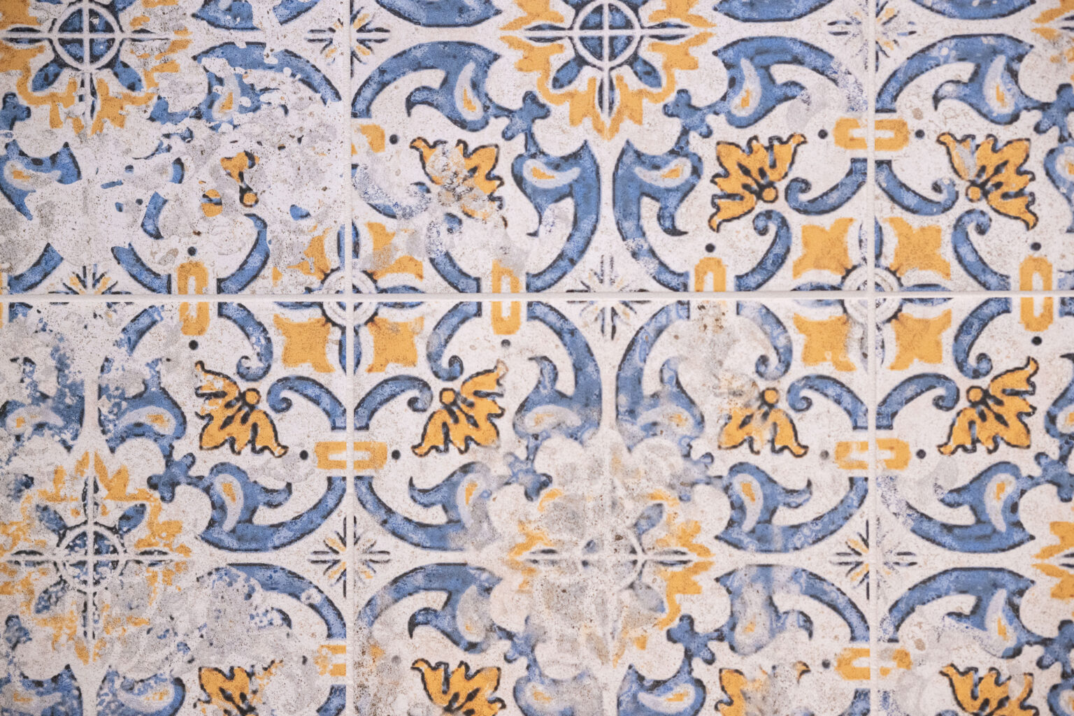Blue and yellow ornate ceramic tiles with intricate floral patterns and weathered surface.