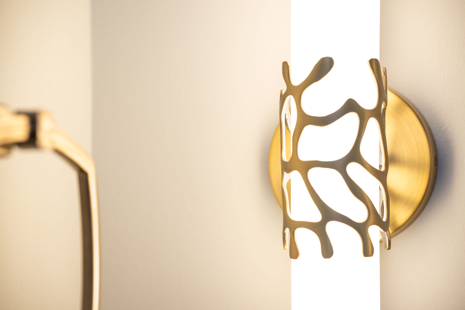 Modern wall sconce with a gold, abstract metal design enclosing a lit, cylindrical white light fixture mounted on a wall.