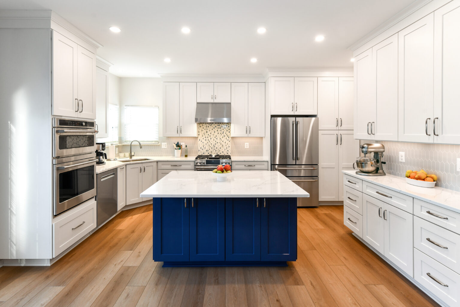 100-Shakley-DSC_2047-2 A modern kitchen with white cabinets, a blue island, stainless steel appliances, and wooden flooring.