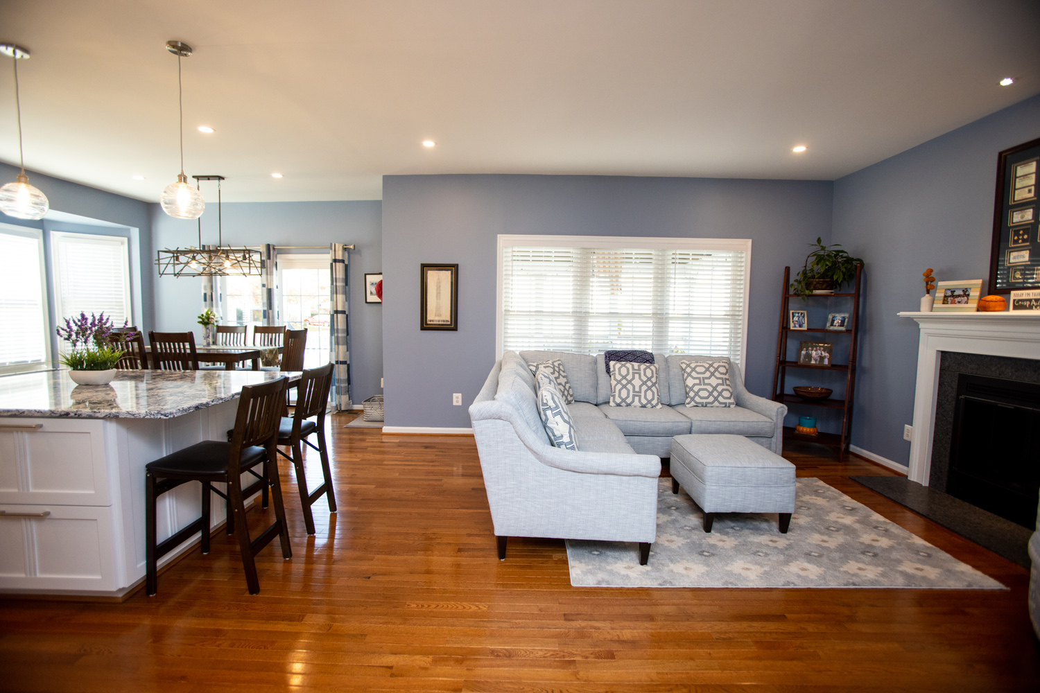 Open-plan living and dining area with light blue walls, hardwood floors, a gray sectional sofa, marble kitchen island, and modern decor.