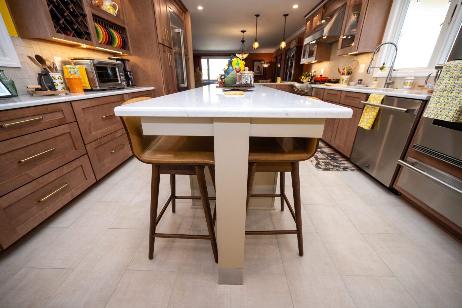 Image by Lesnick Photo Modern kitchen with wooden cabinets, a white island countertop, two wooden chairs, stainless steel appliances, and decorative items on the island.