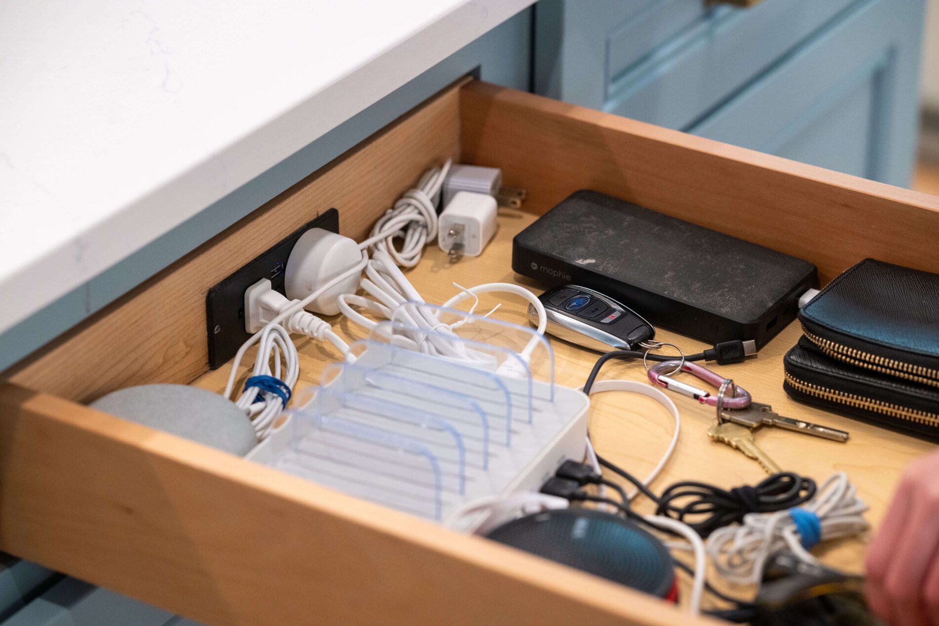 Open drawer containing various charging cables, power adapters, a charging station, a wallet, keys, and small electronic devices—perfect for organizing essentials while pondering how much does a kitchen remodel cost in Northern Virginia.