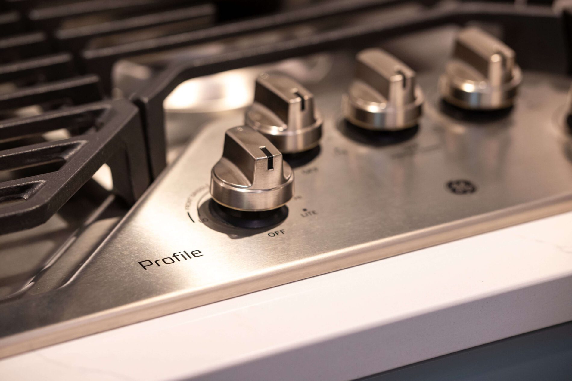 Close-up of four stainless steel stove knobs on a GE Profile gas cooktop, with part of the burner grate visible—an essential detail to consider when estimating how much a kitchen remodel costs in Northern Virginia.