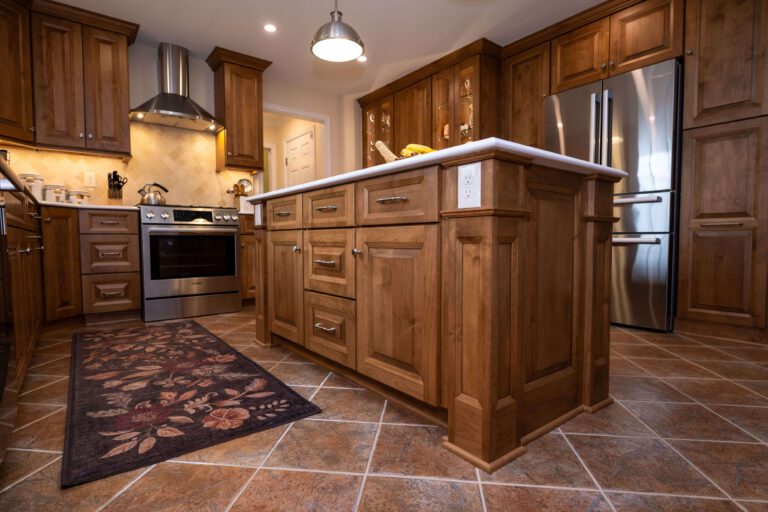 A modern kitchen with wooden cabinets, a central island with drawers, stainless steel appliances, and a patterned rug on a tiled floor—perfect inspiration when considering how much does a kitchen remodel cost in Northern Virginia.