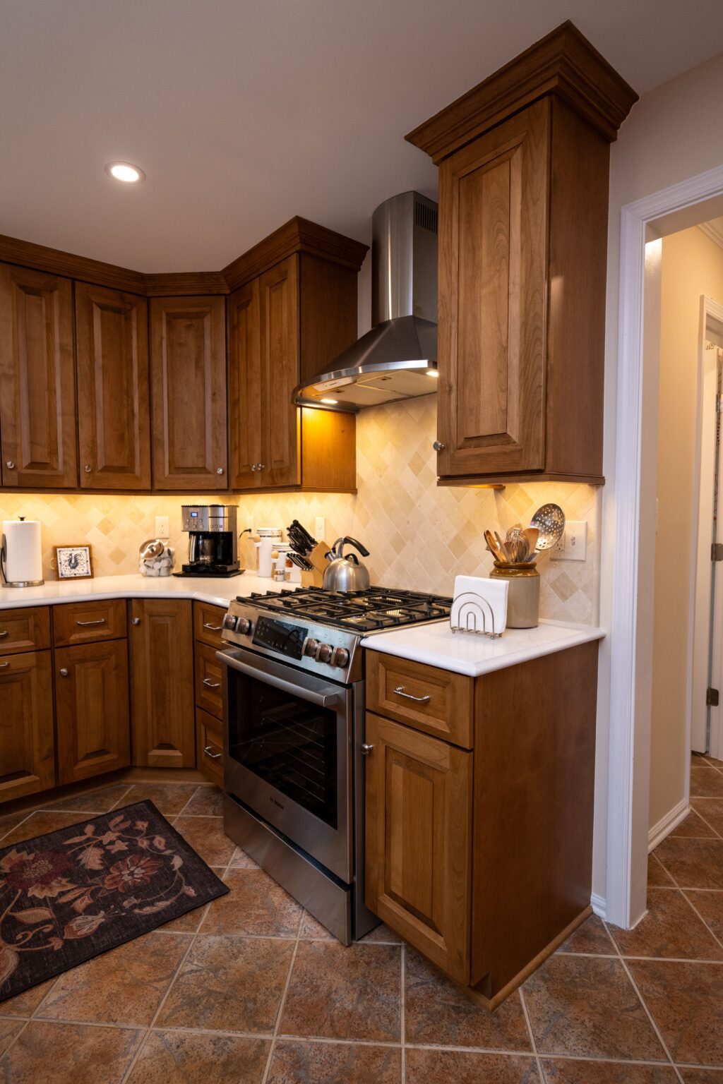 A kitchen with wooden cabinets, stainless steel stove, oven, and range hood, countertop appliances, and tile flooring.
