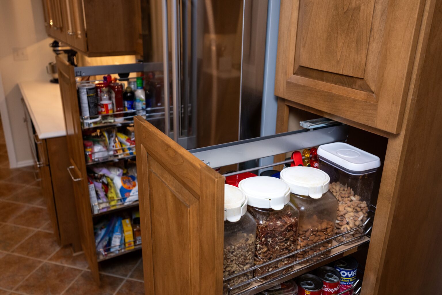 Two kitchen pantry cabinets pulled open, revealing organized shelves with jars of nuts, dry goods, and various packaged food items.
