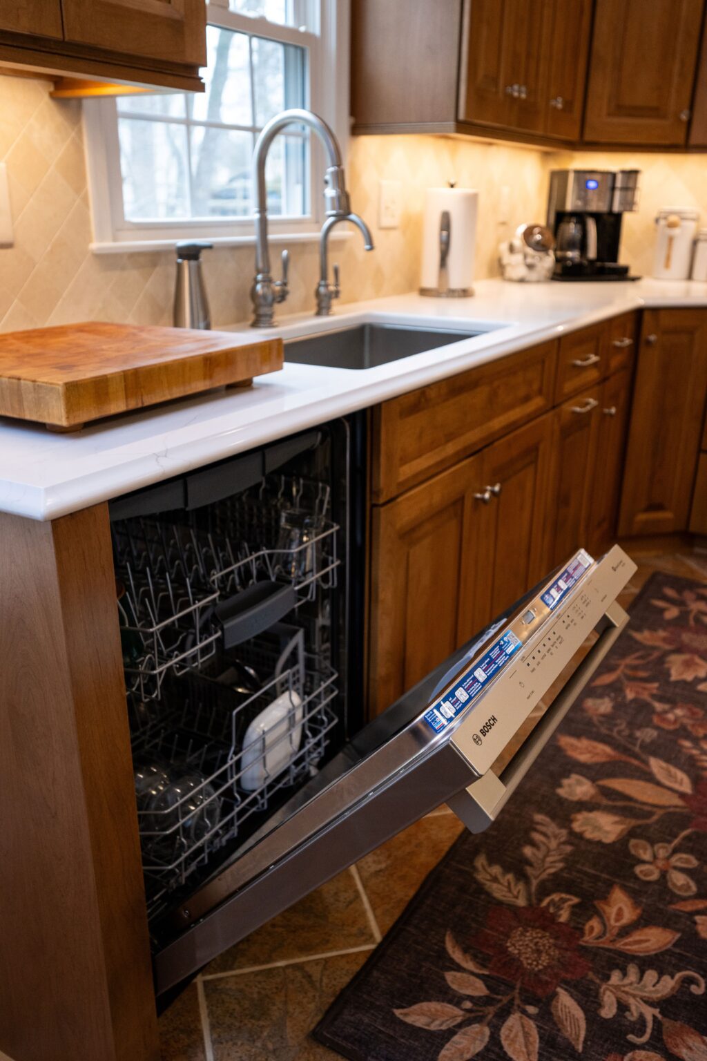 A modern kitchen with wooden cabinets, a sink, and an open Bosch dishwasher partially loaded with dishes.