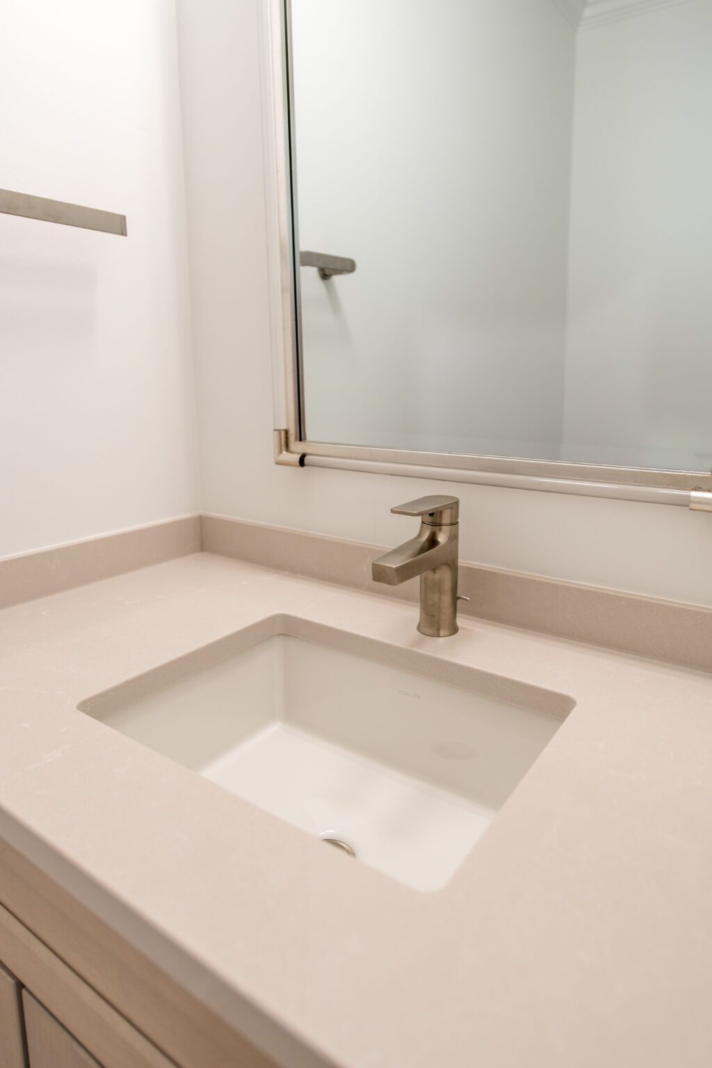 A modern bathroom sink with a rectangular basin, beige countertop, and a metallic faucet, positioned below a wall-mounted mirror.
