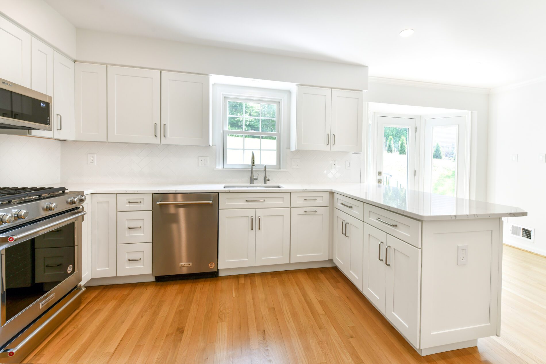 Modern kitchen with white cabinets, stainless steel appliances, a large window above the sink, and light wood flooring.