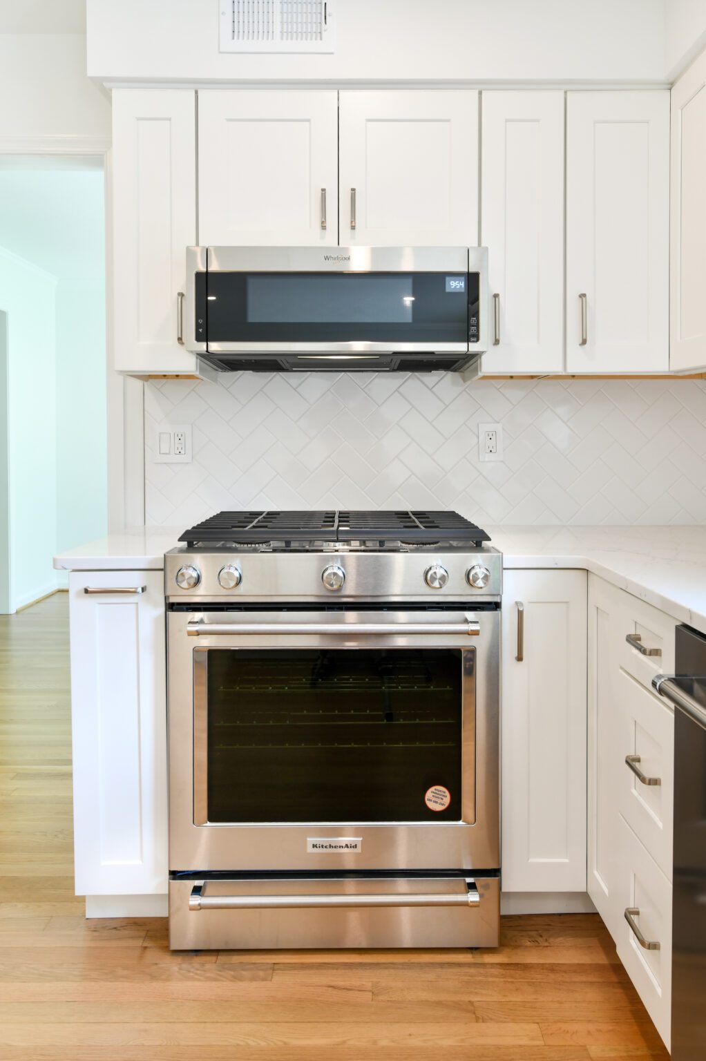 Stainless steel oven with gas cooktop and built-in microwave above, set in a modern kitchen with white cabinets and herringbone tile backsplash.