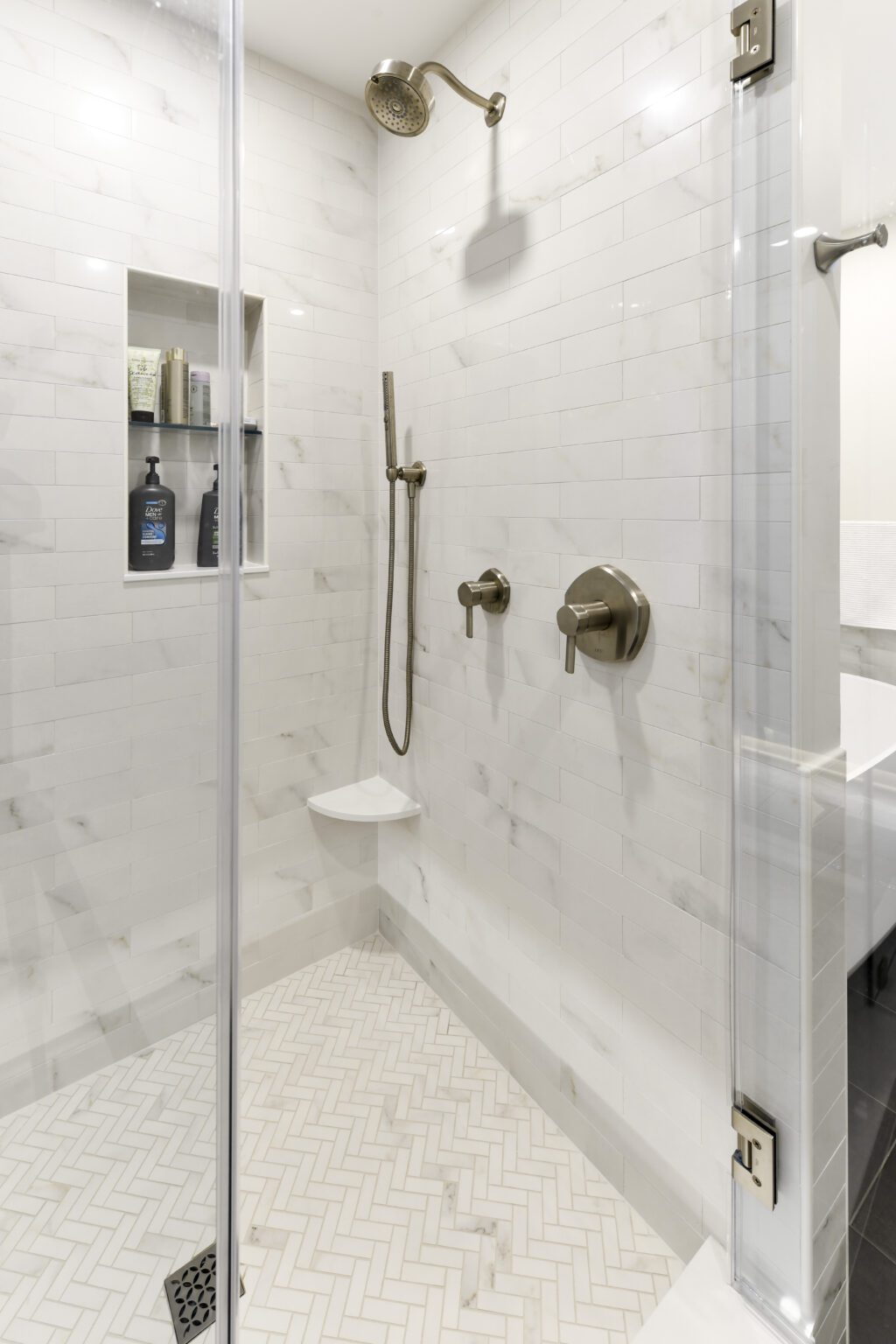 Vienna Primary En-suite and Laundry (14) Modern shower with white tile walls and herringbone-patterned floor, featuring a rainfall showerhead, handheld shower, built-in shelf, and glass door.