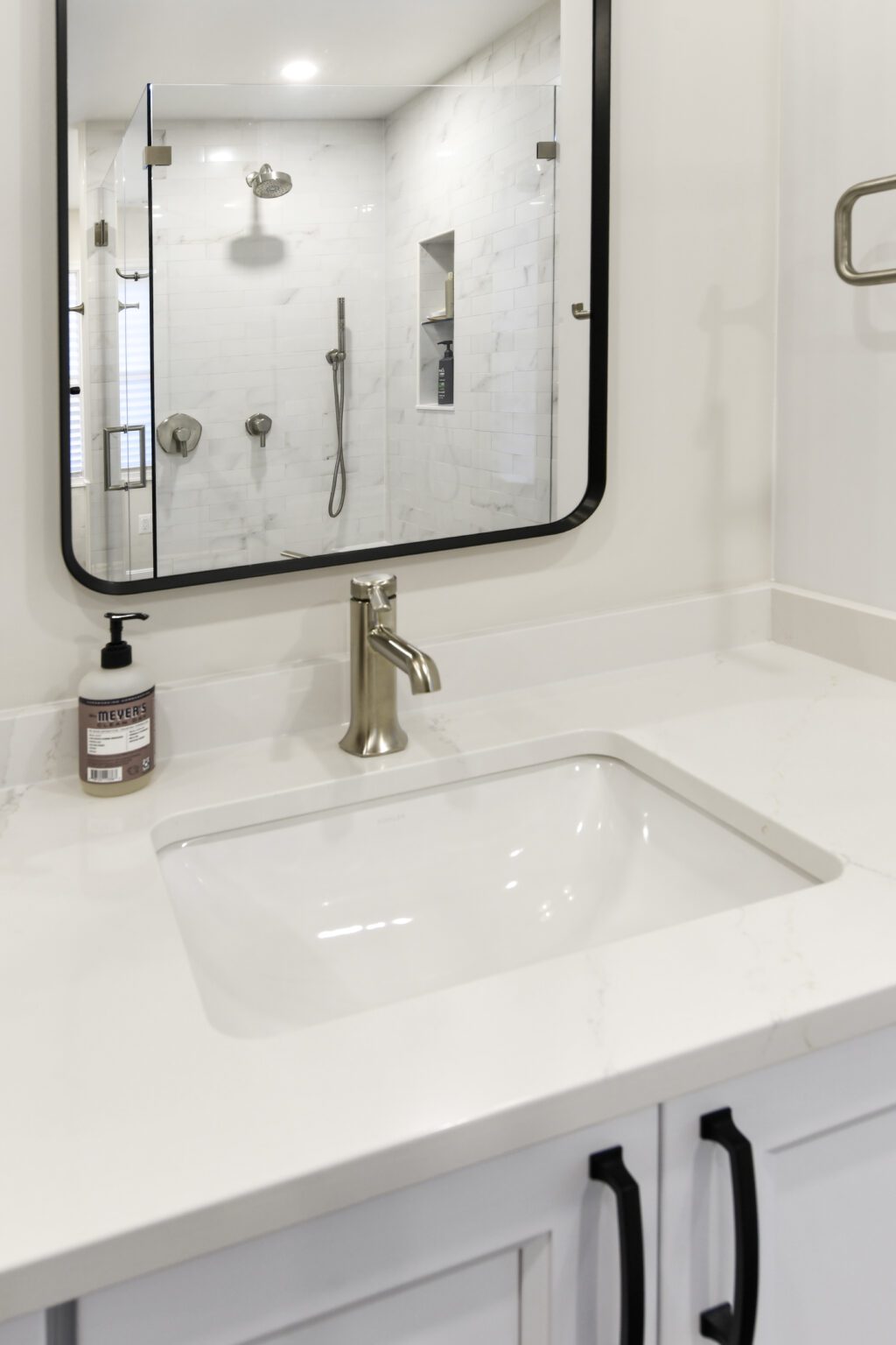 Vienna Primary En-suite and Laundry (2) Modern bathroom vanity with a rectangular sink, silver faucet, soap dispenser, and large mirror; walk-in shower with glass door visible in the reflection.