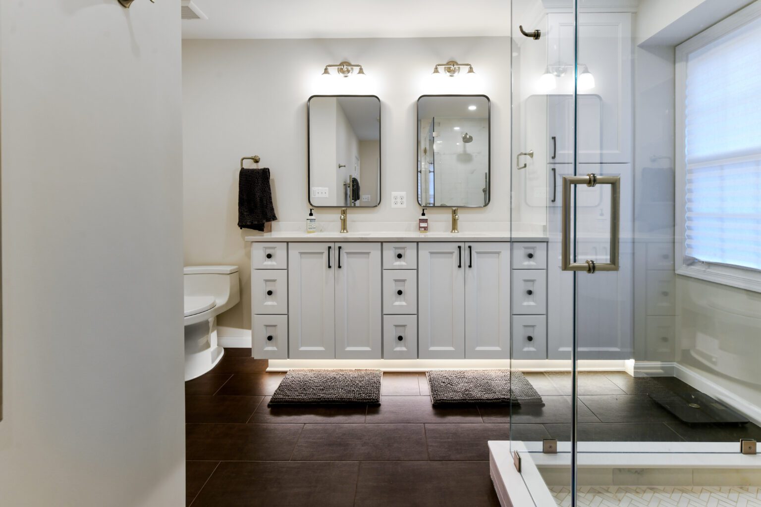 Vienna Primary En-suite and Laundry (9) Modern bathroom with double sinks, rectangular mirrors, white cabinets, dark floor tiles, a glass shower enclosure, and a toilet in the corner.