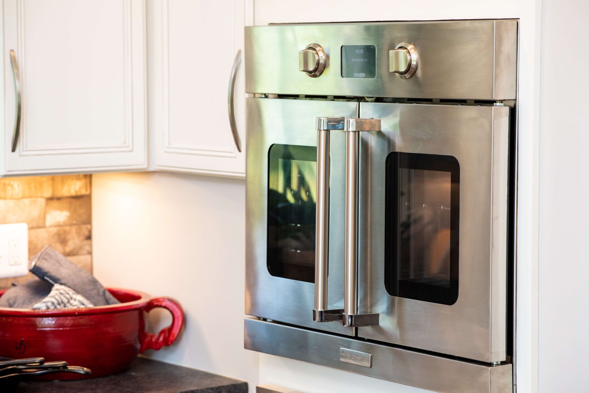 Stainless steel double oven with French doors, an excellent choice among aging in place products, installed in a modern kitchen with white cabinets and a red dish on the counter.