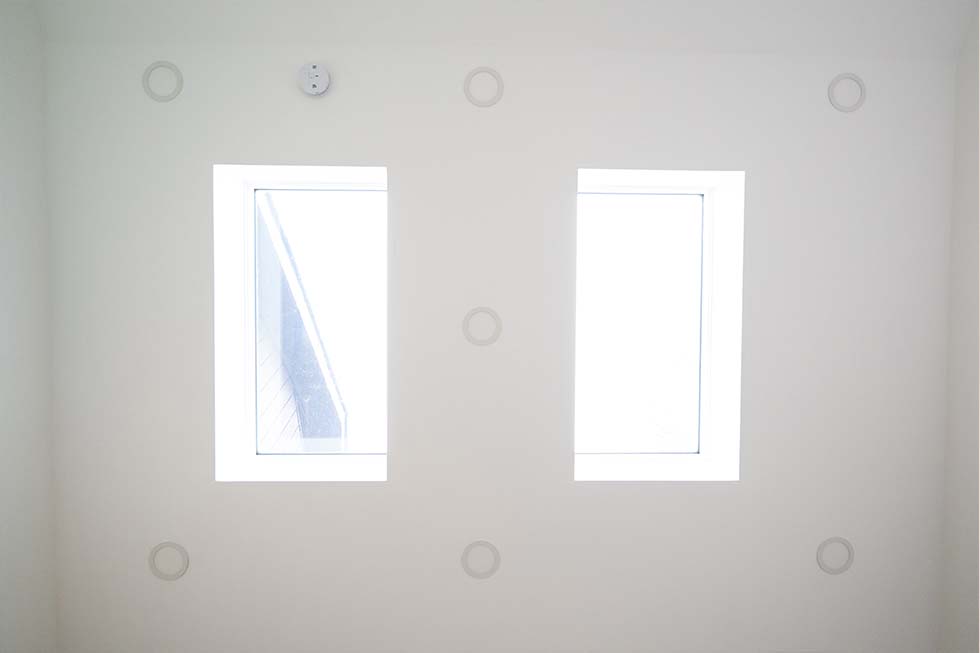 Two rectangular windows on a white wall with a smoke detector above and circular markings surrounding the windows.