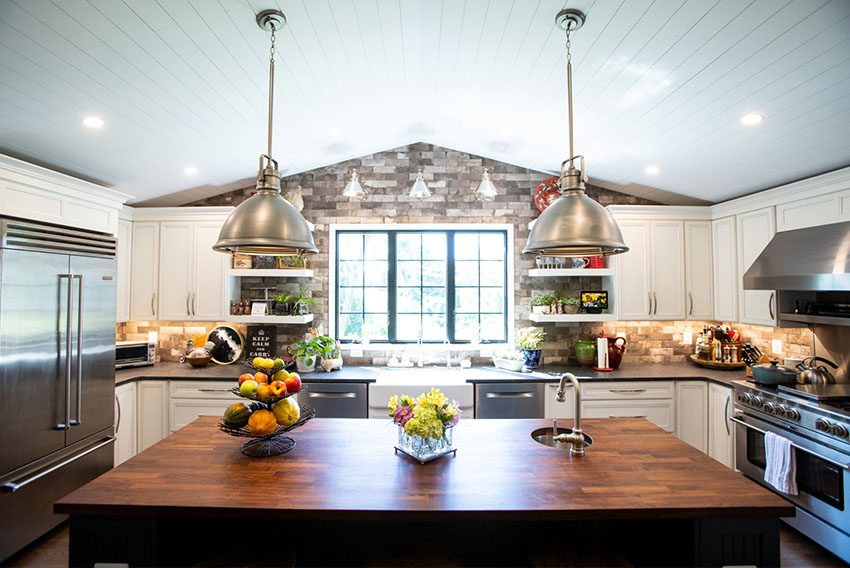 Modern kitchen with a large wooden island, stainless steel appliances, pendant lights, white cabinets, and a window over the sink. Perfect for those considering kitchen remodeling in McLean VA, with a fruit bowl and flowers on the island.