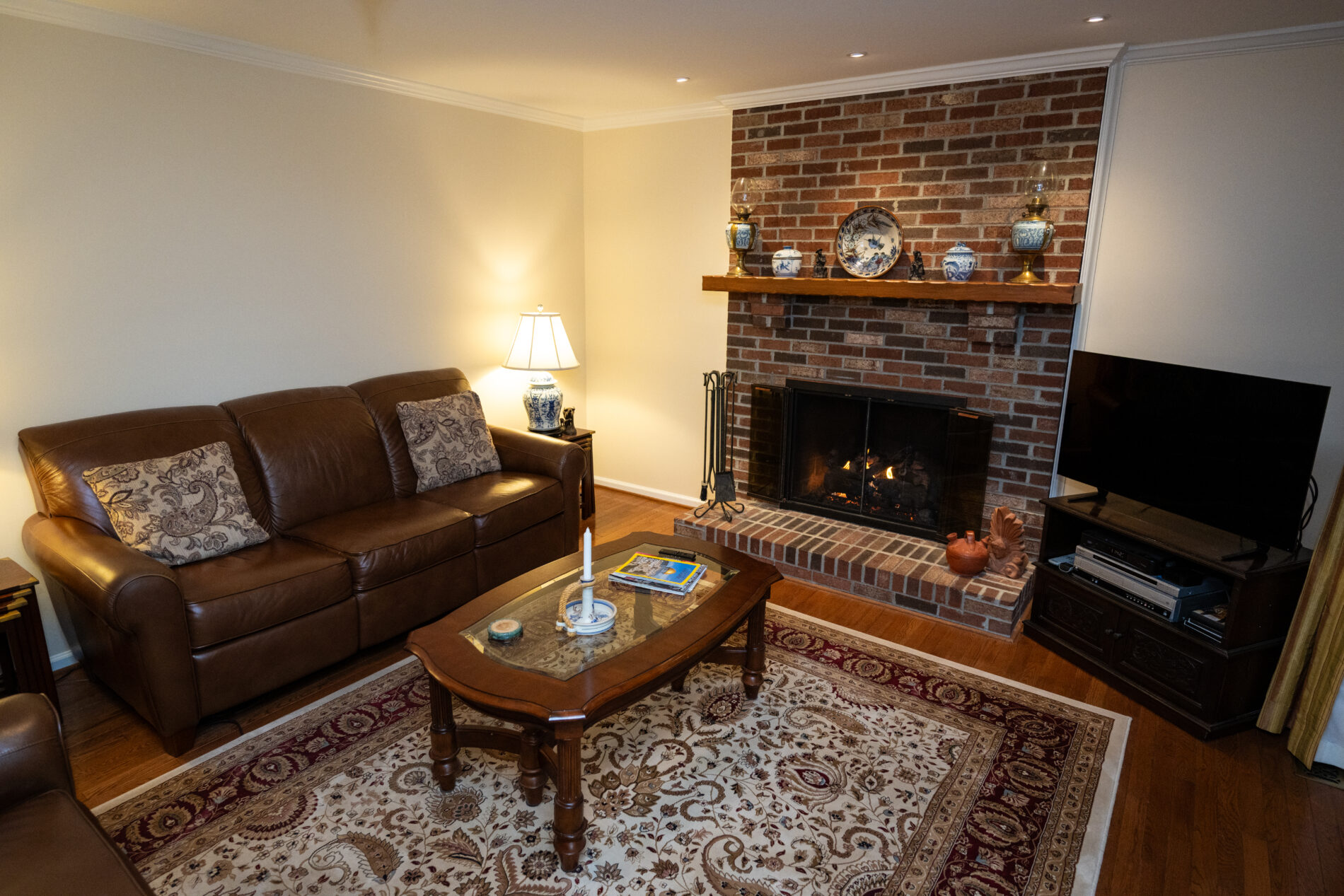 A cozy living room with leather sofas, a wooden coffee table, a patterned rug, and a brick fireplace offers comfort amid rising costs and interest rates in remodeling Northern Virginia. TV sits on a stand for relaxed evenings.
