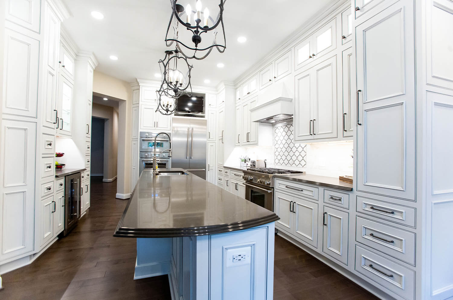 Modern kitchen featuring white cabinets, stainless steel appliances, dark countertops, and pendant lighting over a long central island—perfect inspiration for your next kitchen remodeling McLean VA project.