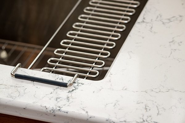 Close-up of a marble-patterned kitchen countertop with a built-in metal dish rack and a horizontal cabinet handle.