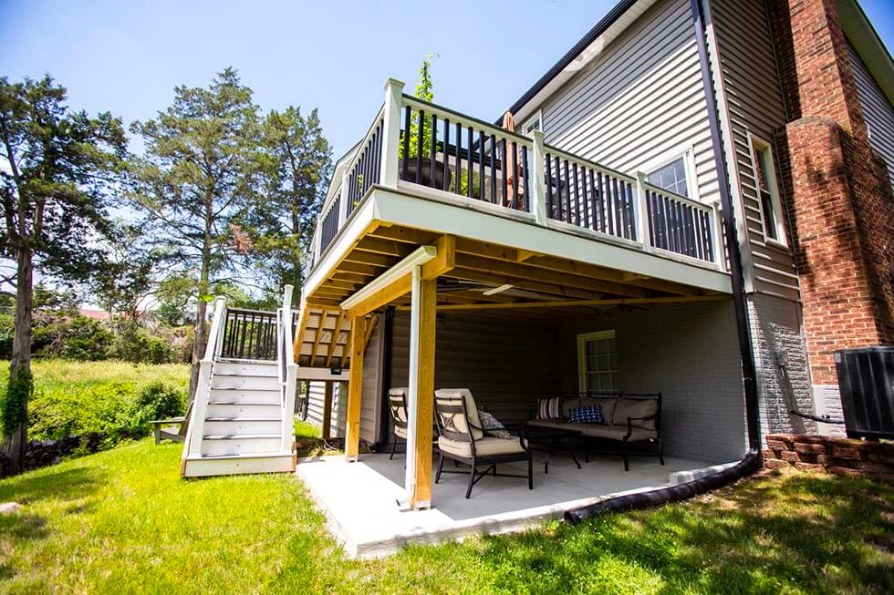 Two-level outdoor deck attached to a house, with stairs leading to an upper seating area and a shaded patio with furniture underneath.