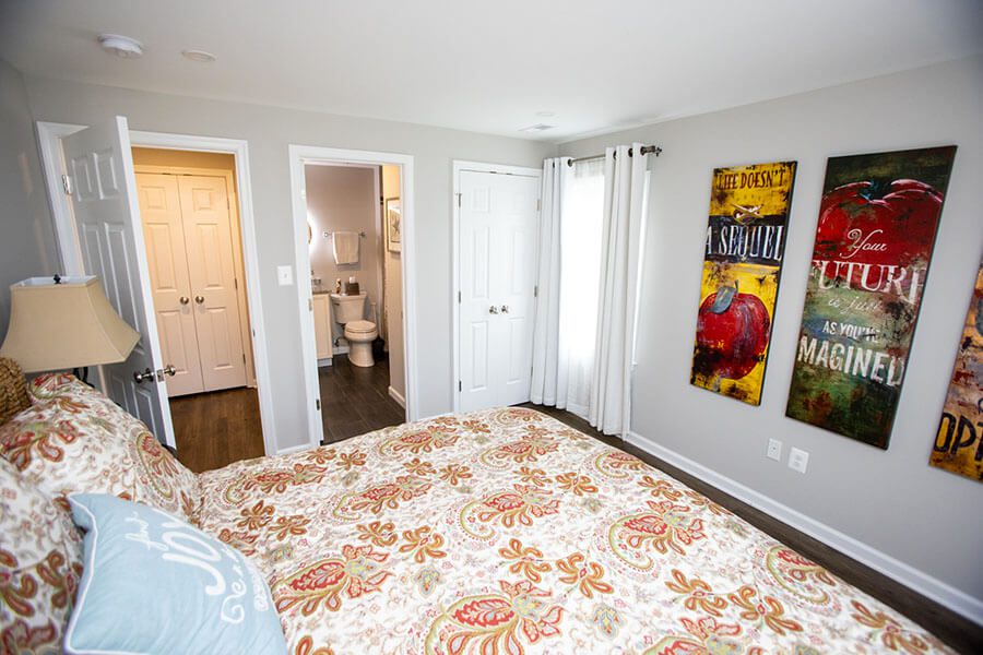 A bedroom with a patterned bedspread, three colorful wall art pieces, an open door to a bathroom, and two closed white doors—perfect inspiration for home additions Vienna VA homeowners will love.
