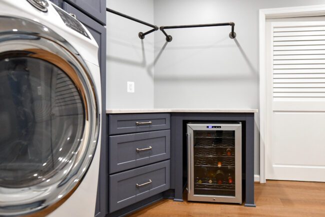 Laundry room with blue cabinets, stainless steel washer, a small wine fridge under the counter, and a wall-mounted hanging rod.