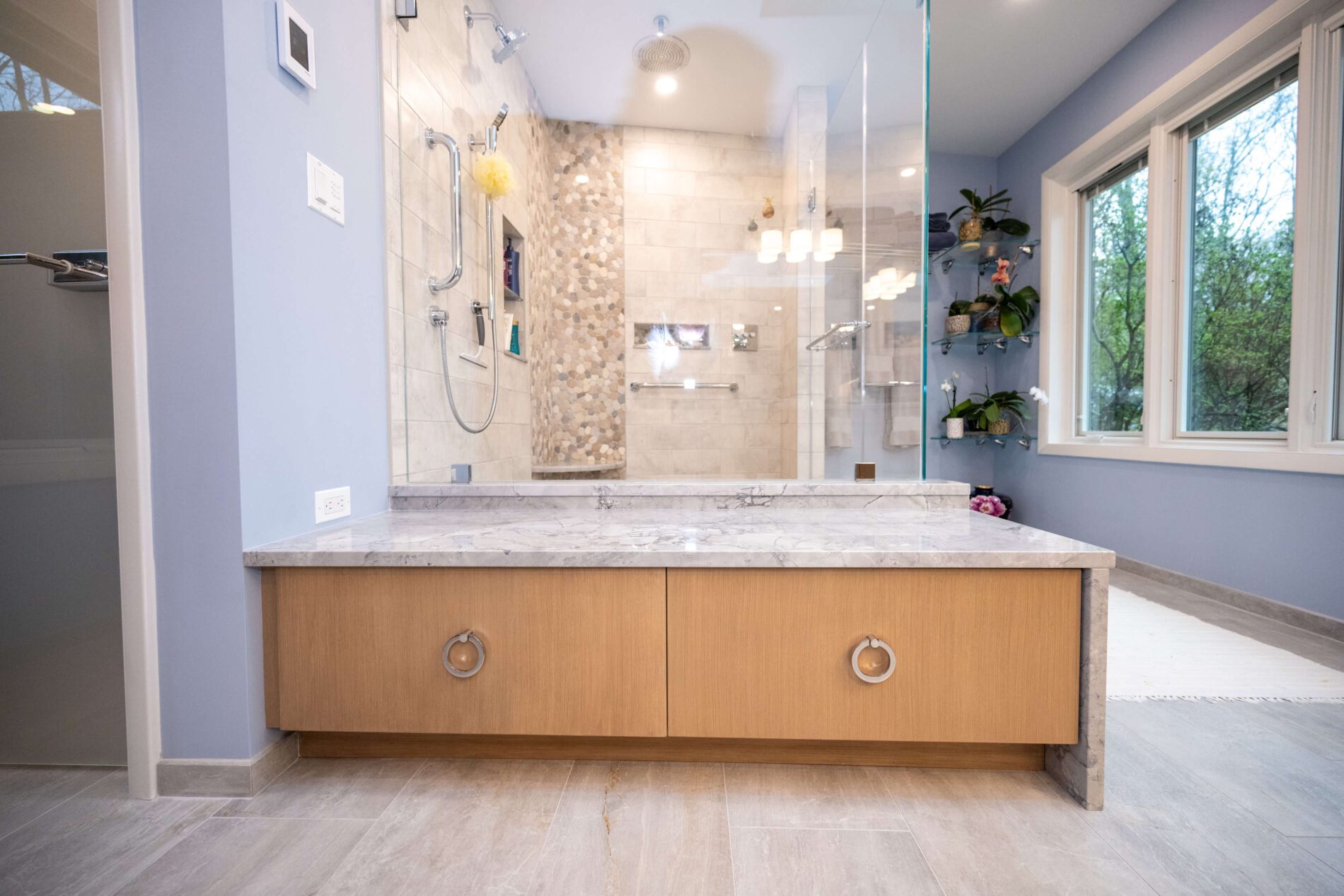 Modern bathroom with a built-in wooden vanity, a glass-enclosed shower with tiled walls, and large windows letting in natural light.