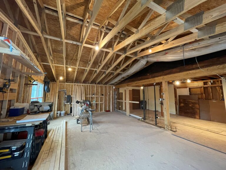 Unfinished interior of a building under construction with exposed wooden framing, work lights, tools, and construction materials scattered around—making you consider where to stay during a renovation.