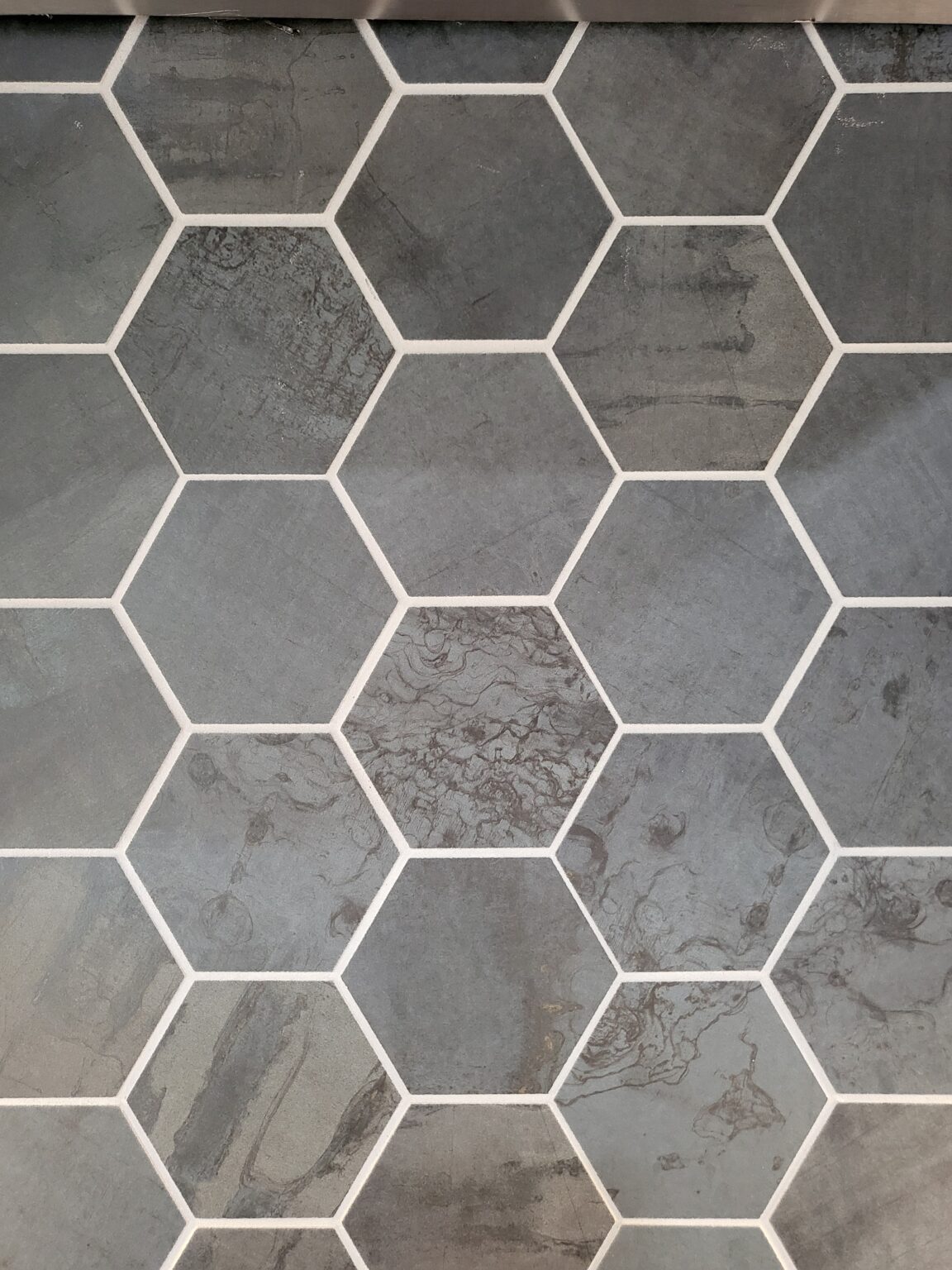 A close-up view of gray hexagonal tiles with white grout lines, showing slight variations in texture and shade across the surface.